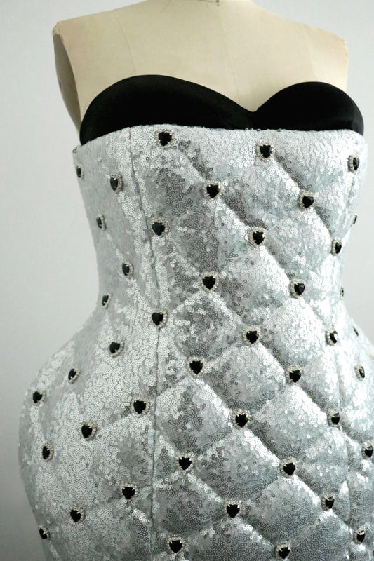 Black sweetheart strapless top tucked into textured silver sequin quilt dress with rhinestone heart detail on sequin quilt pattern on a mannequin against a gray background