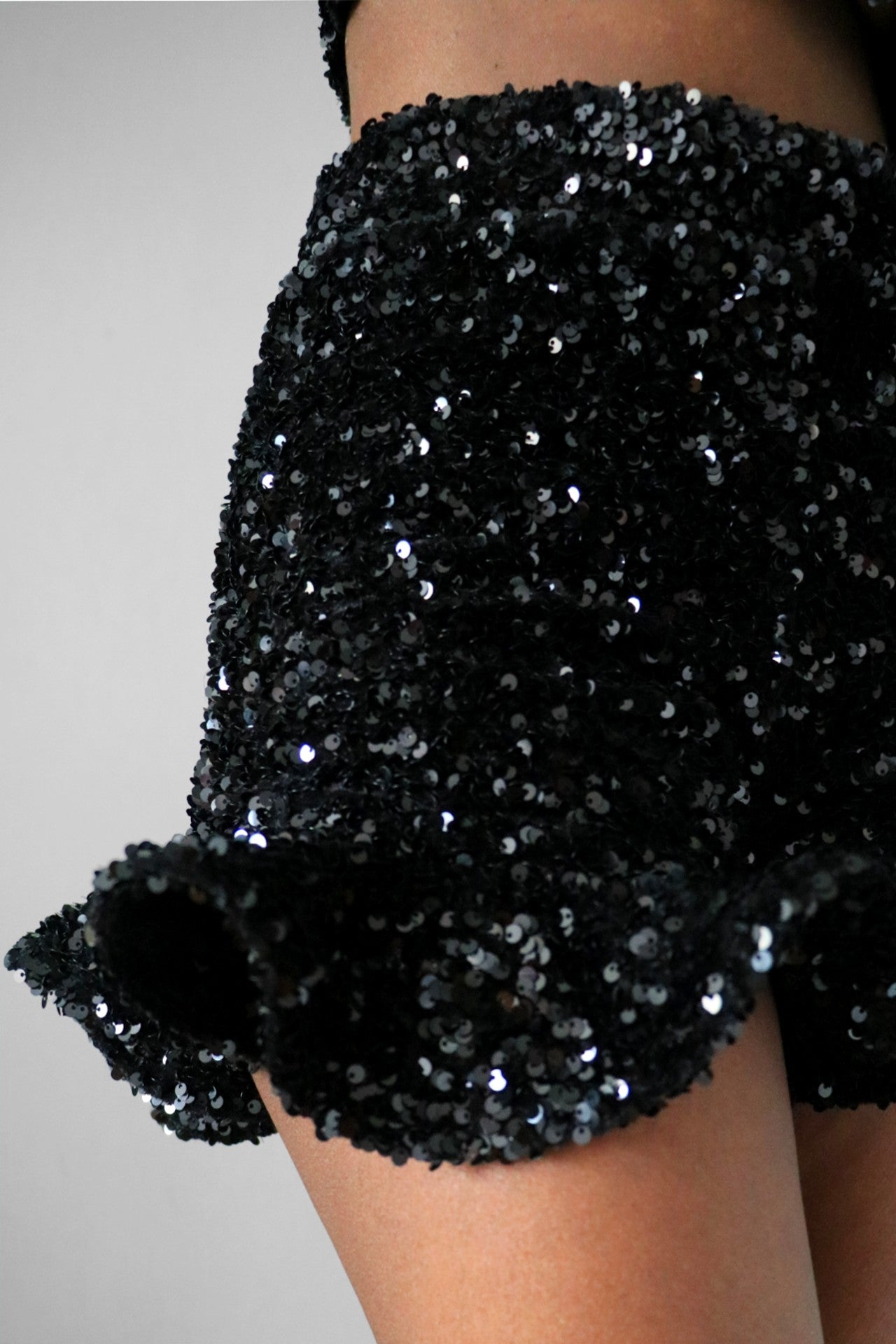 Model wearing detail view of high waist black sequin ruffle shorts