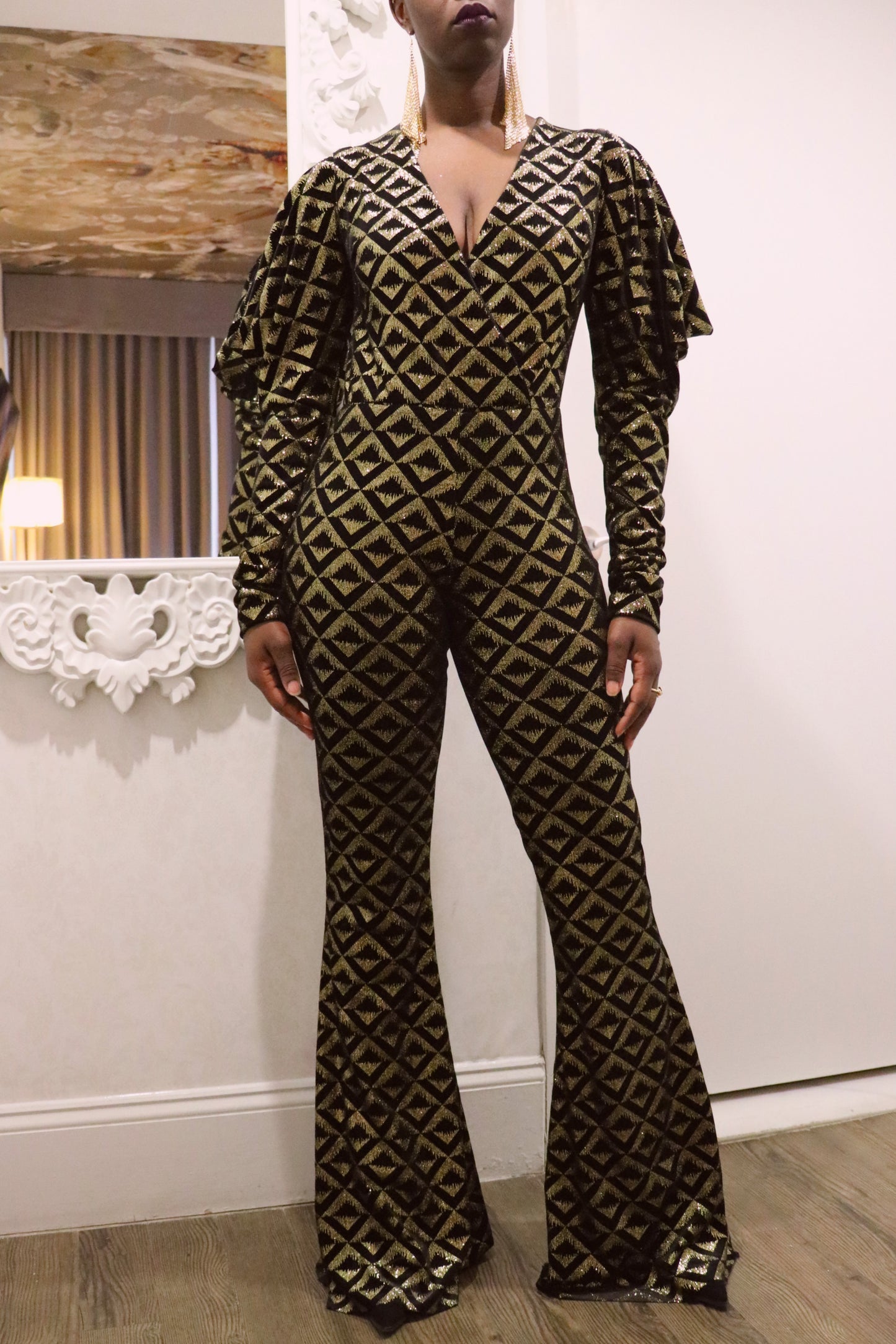 Model wearing a black and gold geometric-patterned jumpsuit in an indoor setting.