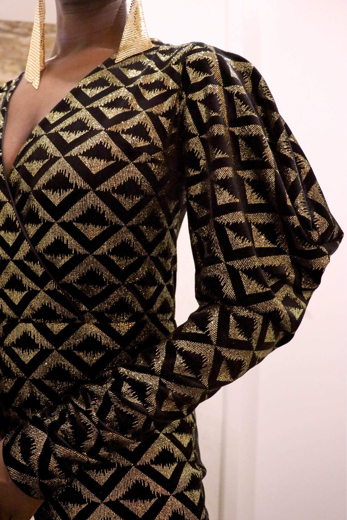 Black and gold geometric-patterned jumpsuit with long sleeves on a plain background