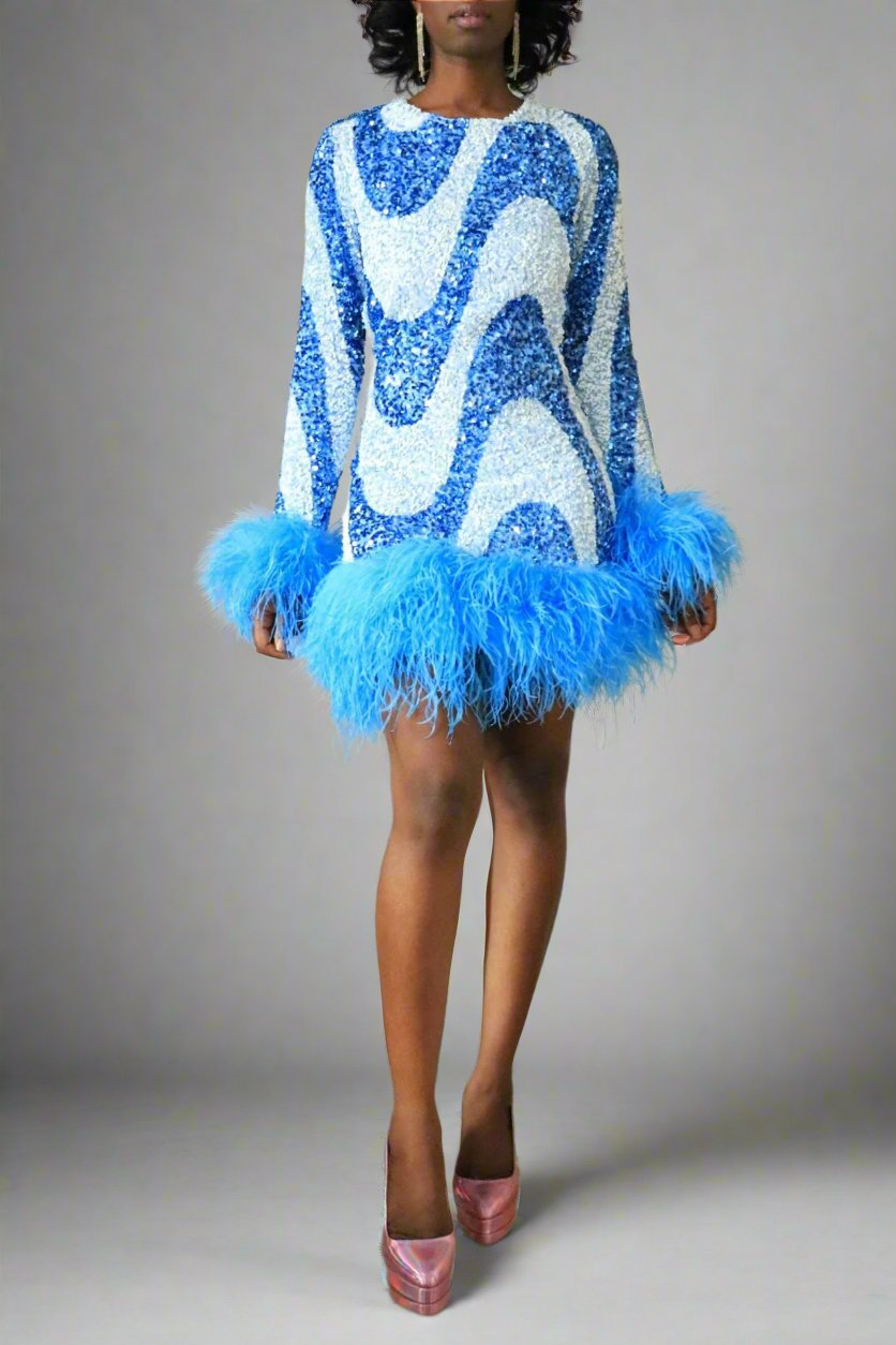 Front view of model wearing blue & white sequin swirl feather dress that is long sleeves with feather trim at hem and cuff