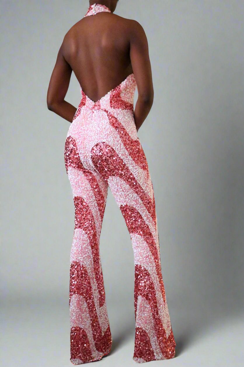 Back view of model wearing a luxury bubblegum pink sequin swirl jumpsuit. The backless halter is a deep v-neckline that stops at the top of the zipper opening at the waistline