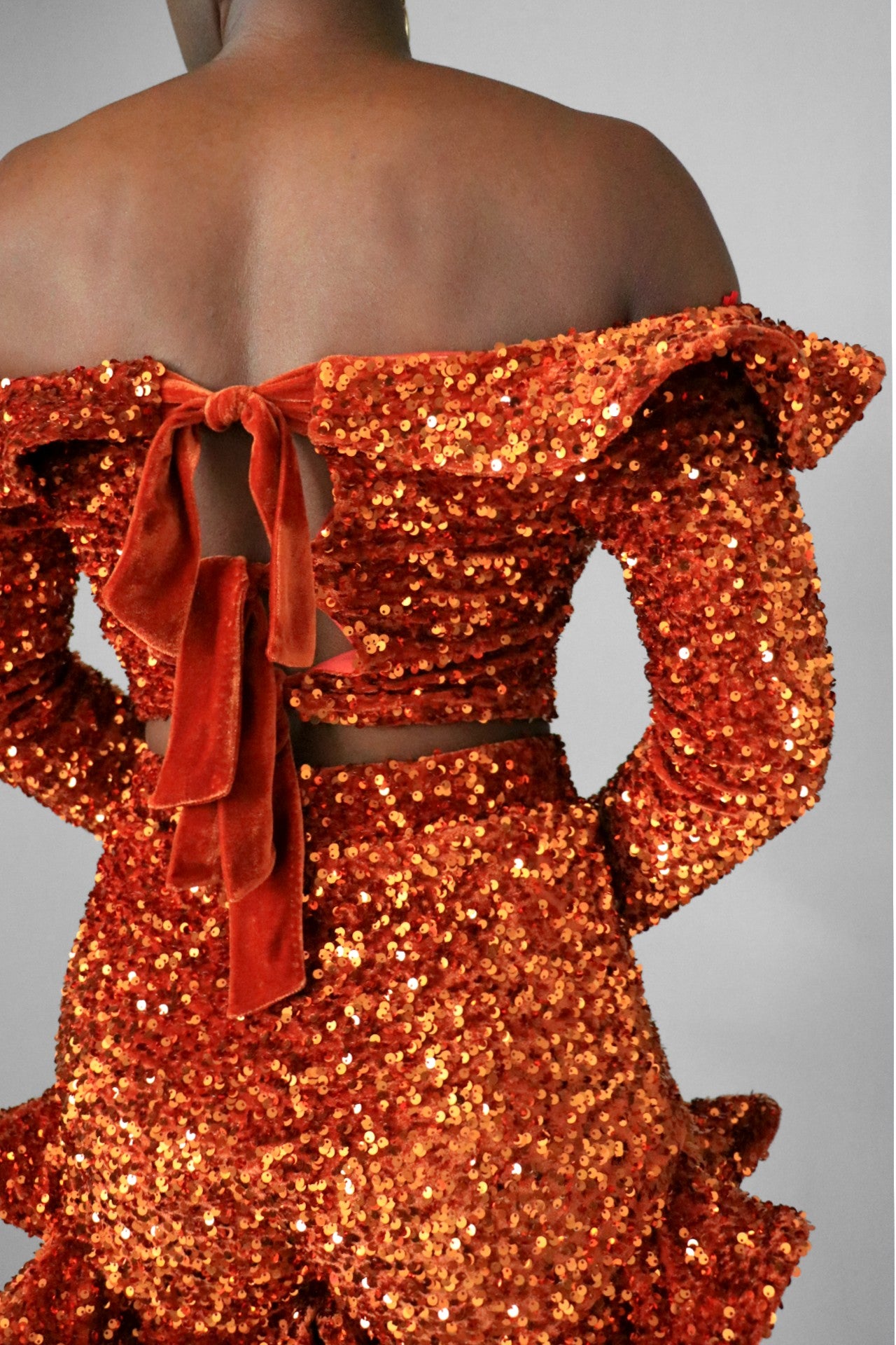 Back view of model wearing burnt orange sequin ruffle off the shoulder crop top