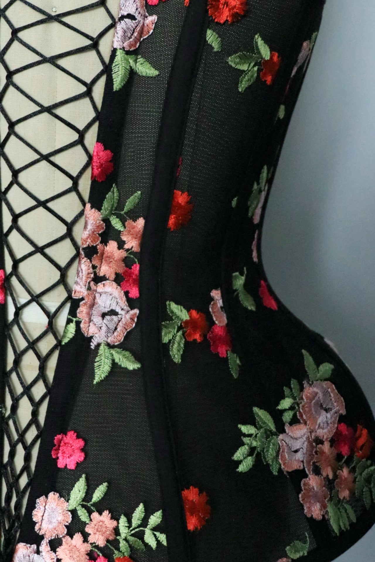 Close-up of a black floral mesh corset with colorful floral embroidery in pink, red, and green, shown.