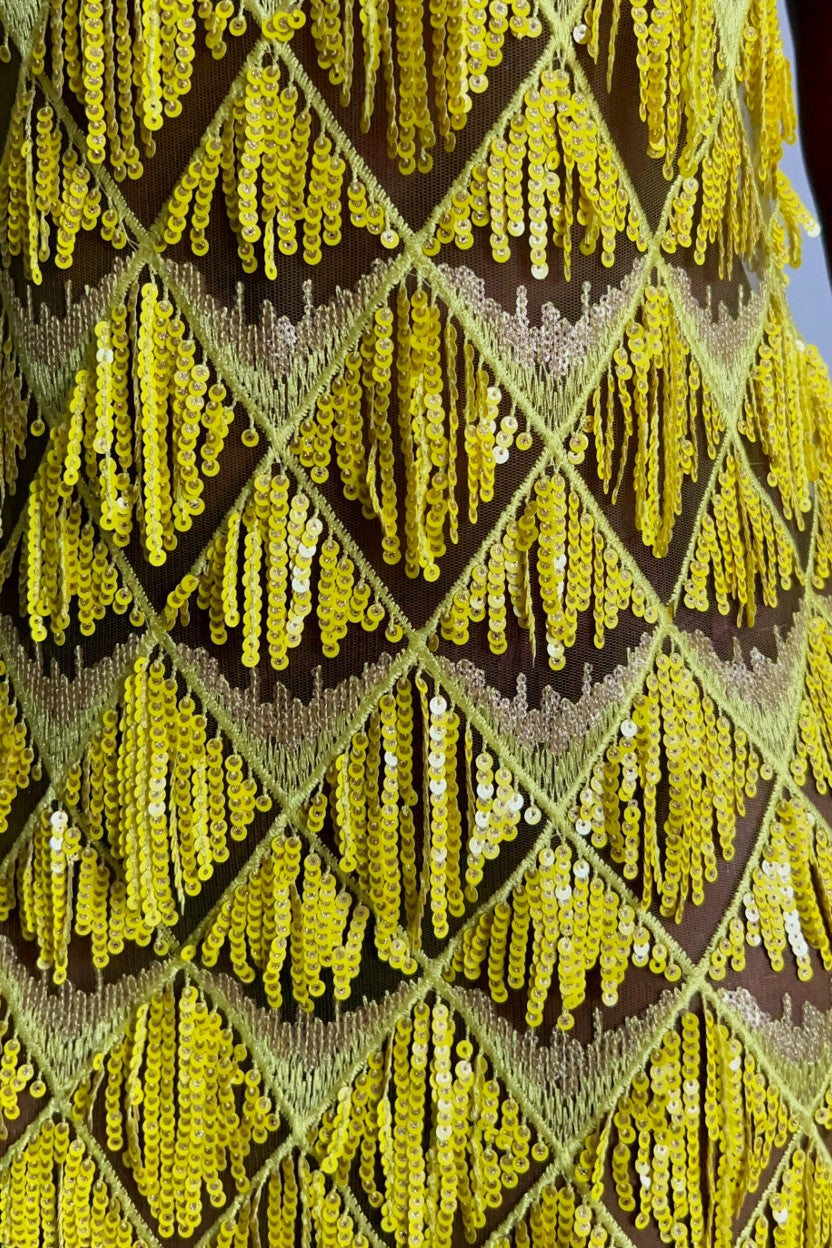 Close-up of a yellow sequined fringe fabric with a repeating diamond pattern 