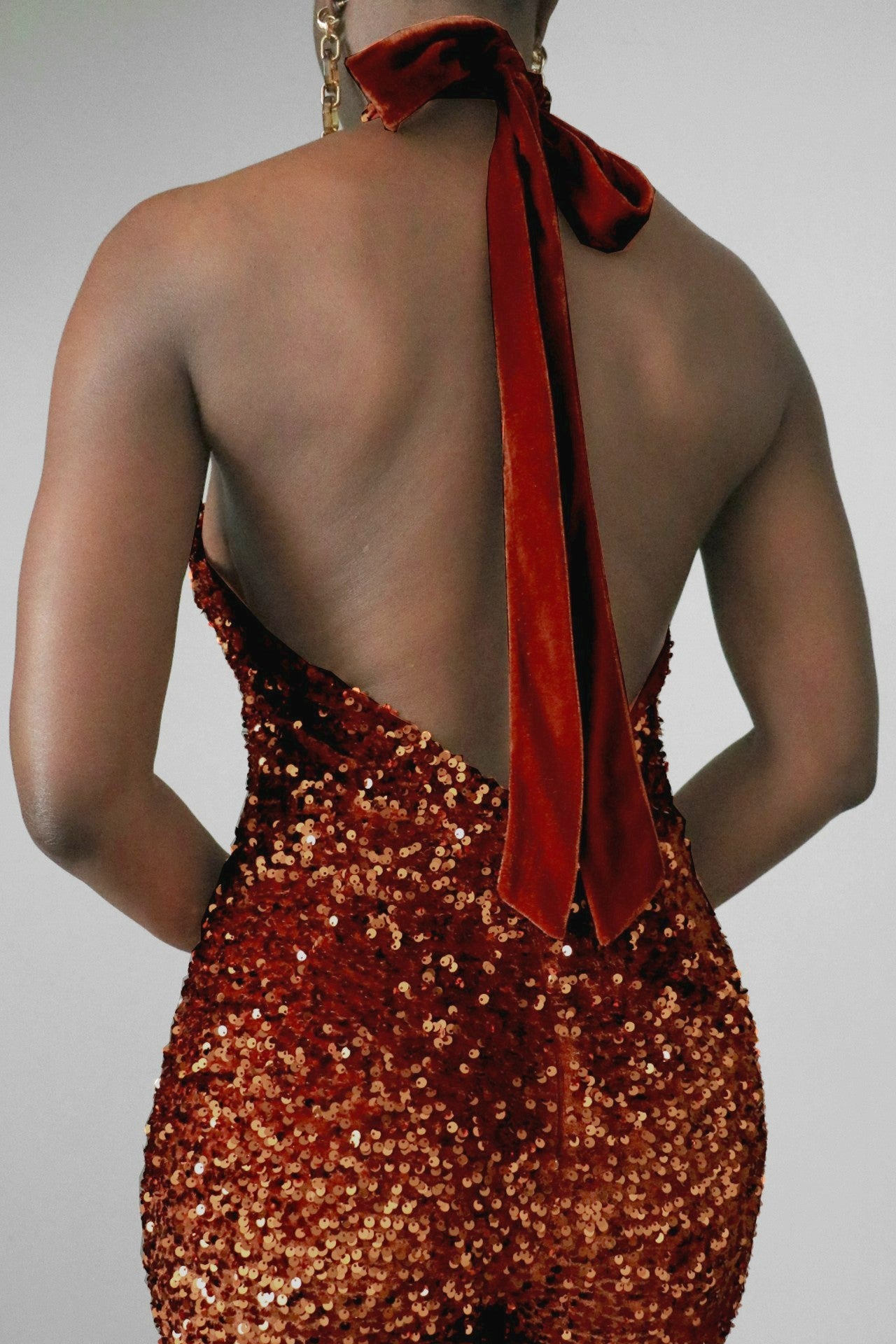 Back close-up of a model wearing a brown sequin halter jumpsuit on a plain background