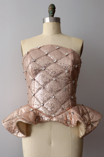 Front view of a rose gold quilted sequin peplum heart rhinestone corset on a dress-form against a gray background