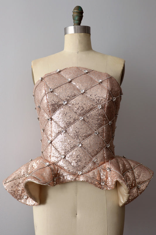 Front view of a rose gold quilted sequin peplum heart rhinestone corset on a dress-form against a gray background