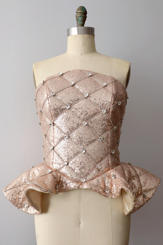 Front view of a rose gold quilted sequin peplum heart rhinestone corset on a dress-form against a gray background
