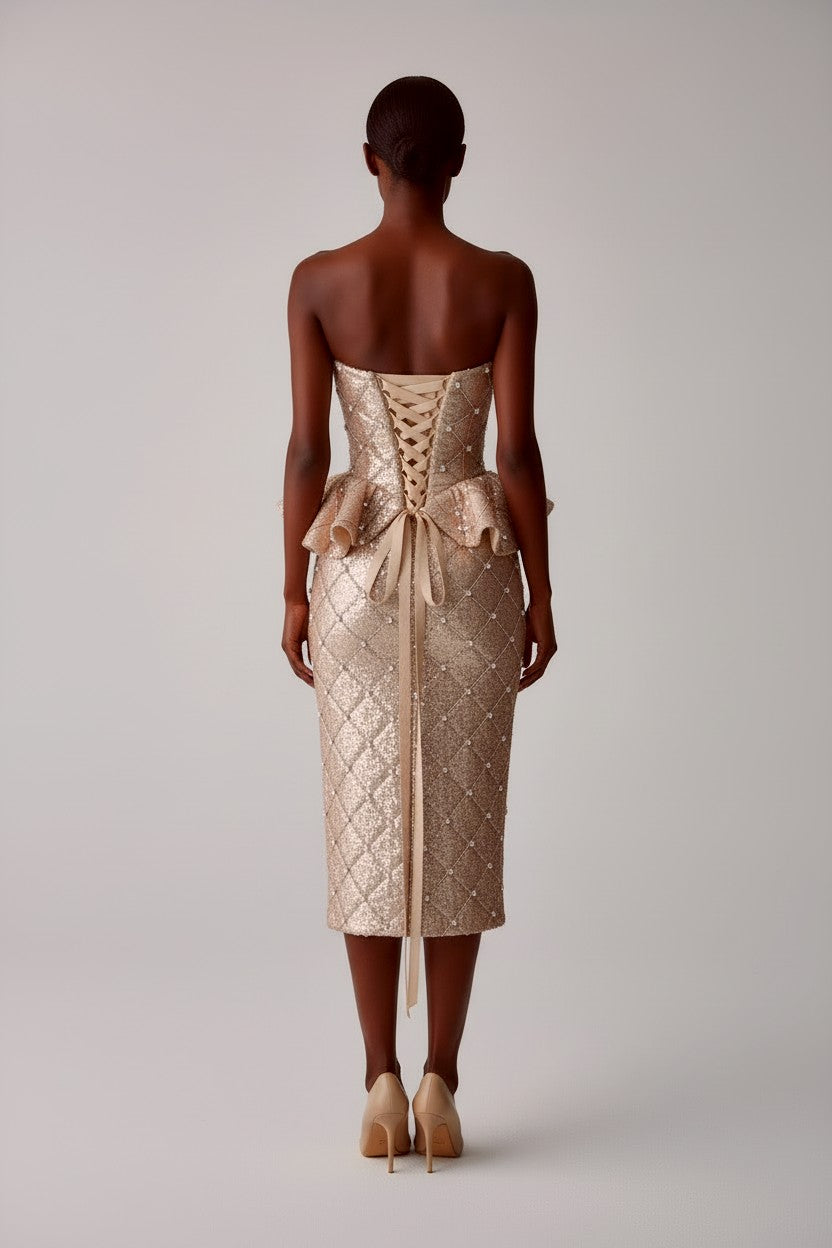 Back view of model wearing a strapless, quilted sequin rhinestone peplum corset with satin lace up ribbon closure and matching midi pencil skirt on a light gray background