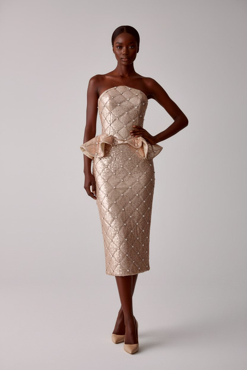 Frontal view of model wearing a strapless, quilted sequin rhinestone peplum corset with a matching midi pencil skirt on a light gray background