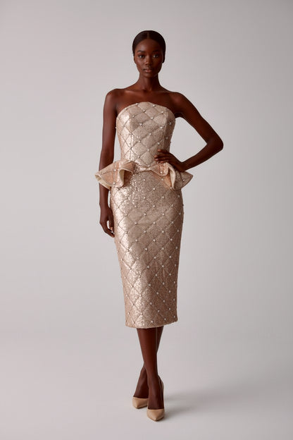 Frontal view of model wearing a strapless, quilted sequin rhinestone peplum corset with a matching midi pencil skirt on a light gray background