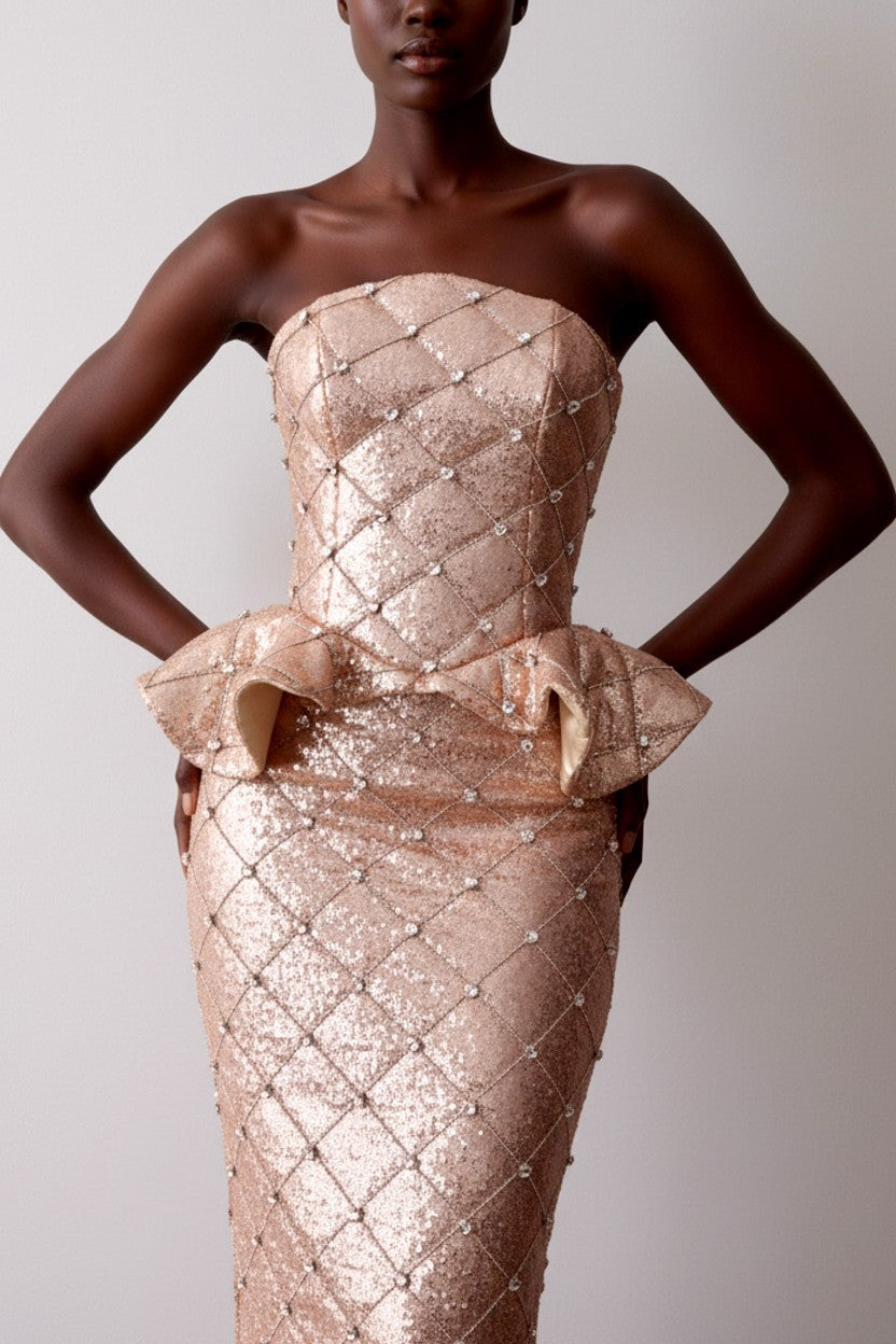 Model wearing a rose gold strapless gown with peplum ruffled detail on a plain background