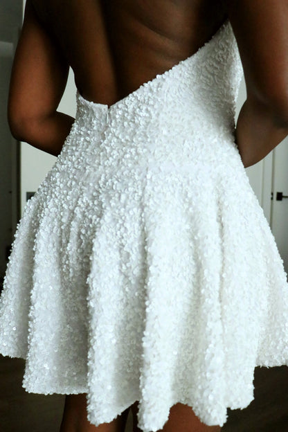 A close-up back view of a model wearing a white textured, sequin mini romper with an open back design.