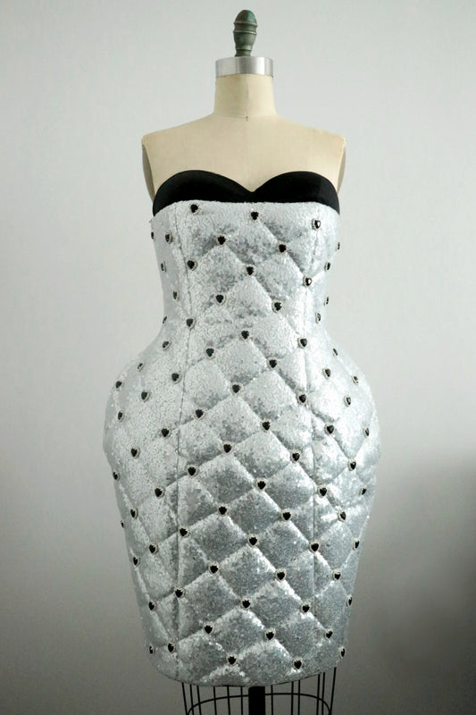 Silver strapless dress with black heart rhinestones bead detailing on a mannequin against a plain background