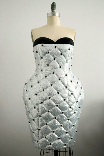 Silver sequin quilted strapless dress with black heart rhinestones bead detailing on a mannequin against a plain background