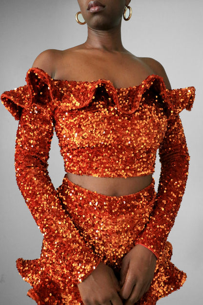 Front view of model wearing burnt orange sequin ruffle off the shoulder crop top
