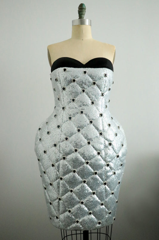 Silver strapless dress with black heart rhinestones bead detailing on a mannequin against a plain background