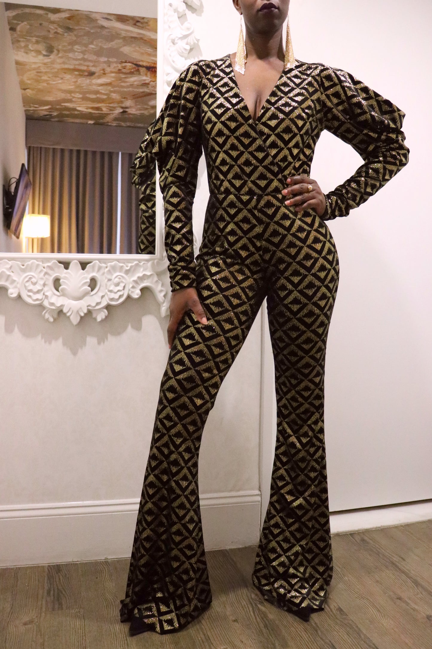 Model wearing a black and gold geometric-patterned jumpsuit in an indoor setting.