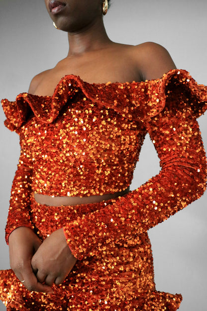 Side front view of model wearing burnt orange sequin ruffle off the shoulder crop top