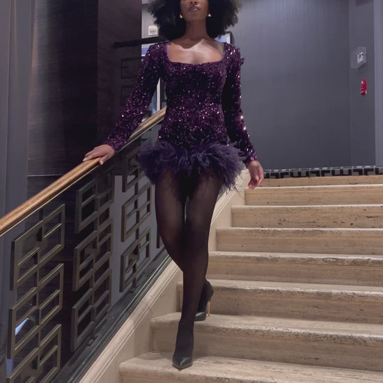 Model walking down the stairs wearing a  purple sequin feather romper