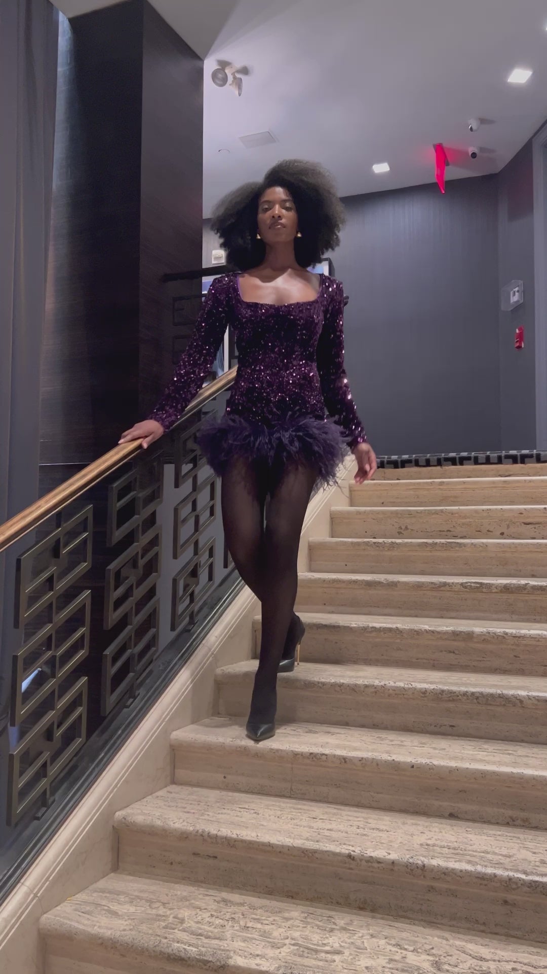 Model walking down the stairs wearing a  purple sequin feather romper